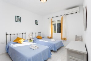 A bedroom with two beds, a bedside table with a lamp, a window with curtains, and a white dresser. - Cortijo Mari Carmen - Three Bedroom Villa, Sleeps 6 (Nerja)