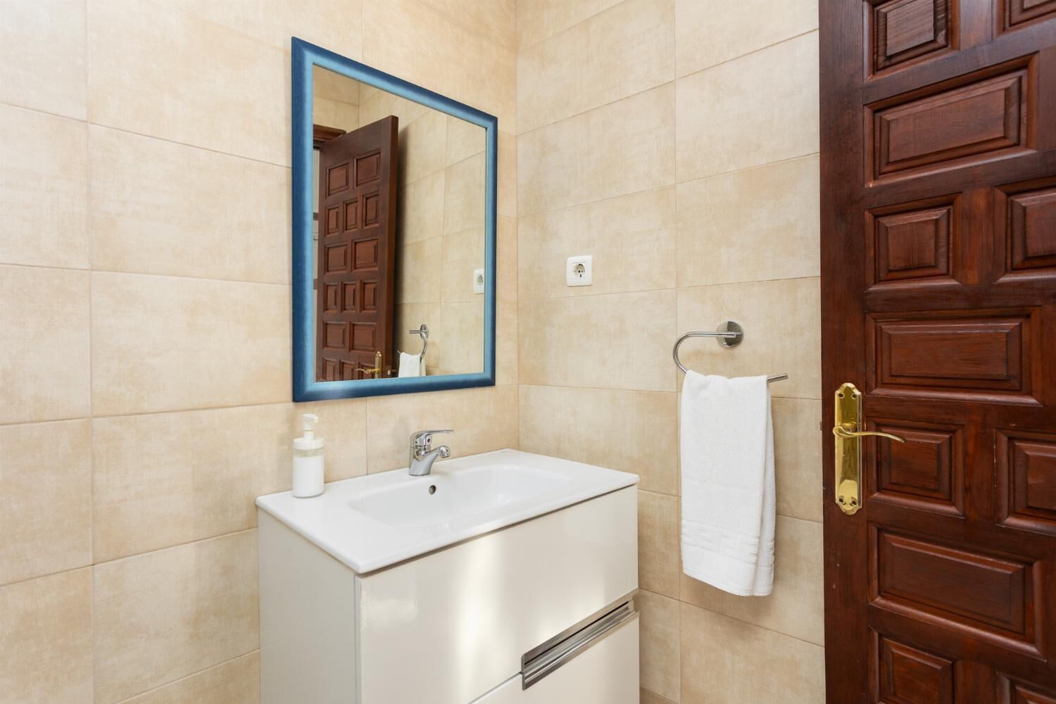 A bathroom with a white sink, a mirror with a blue frame, and a wooden door with a brass handle.