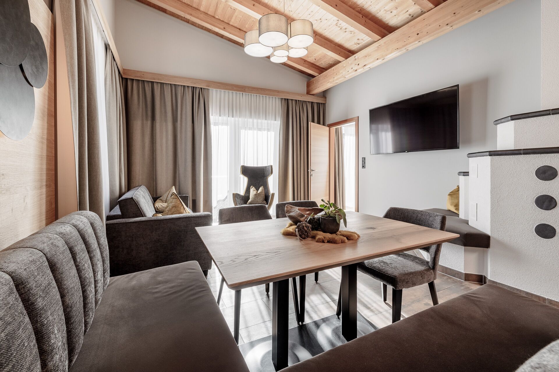 A modern living room with a wooden ceiling, a dining table, sofas, and a TV mounted on the wall.