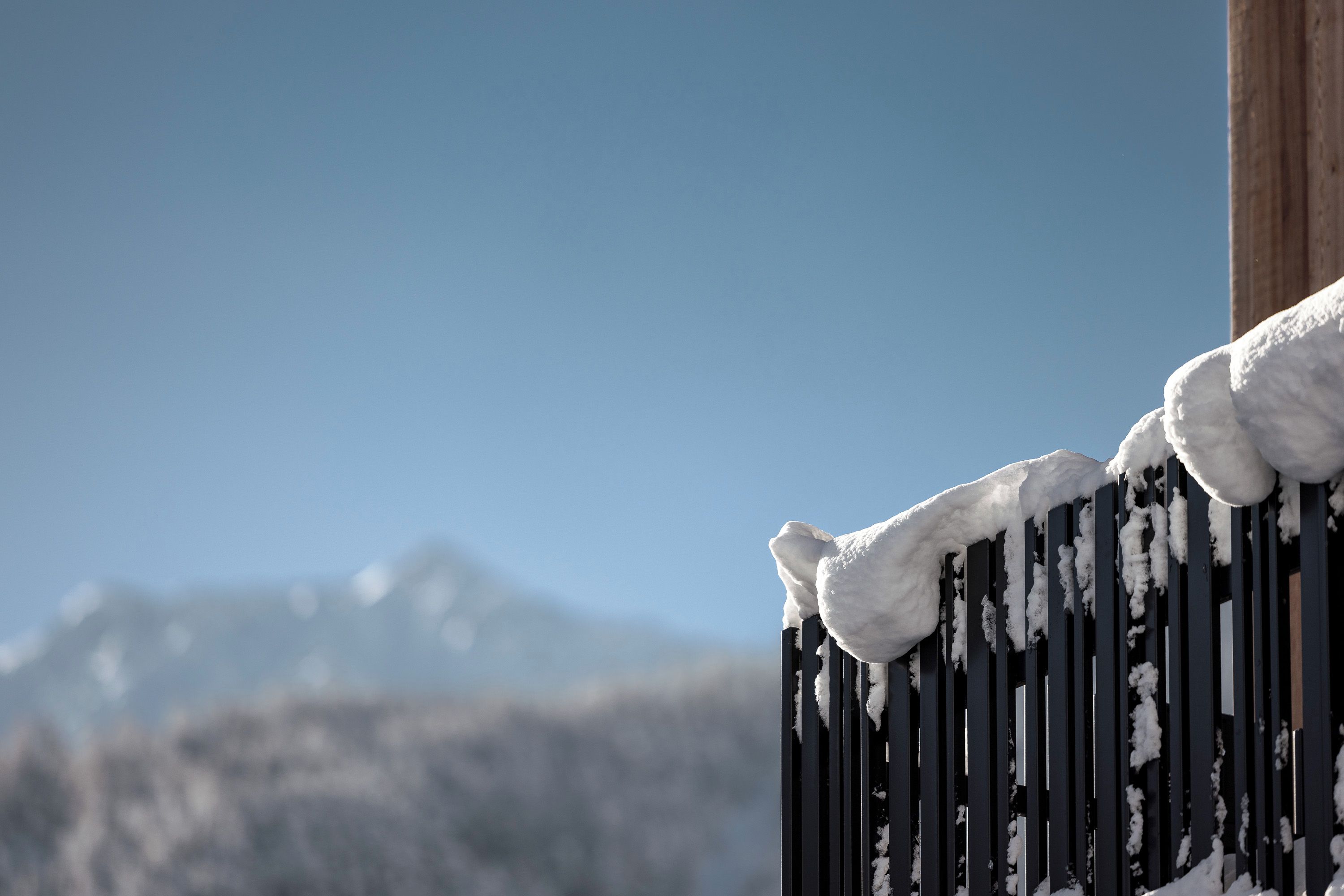 Una valla metálica cubierta de nieve, con un cielo azul despejado y montañas al fondo.