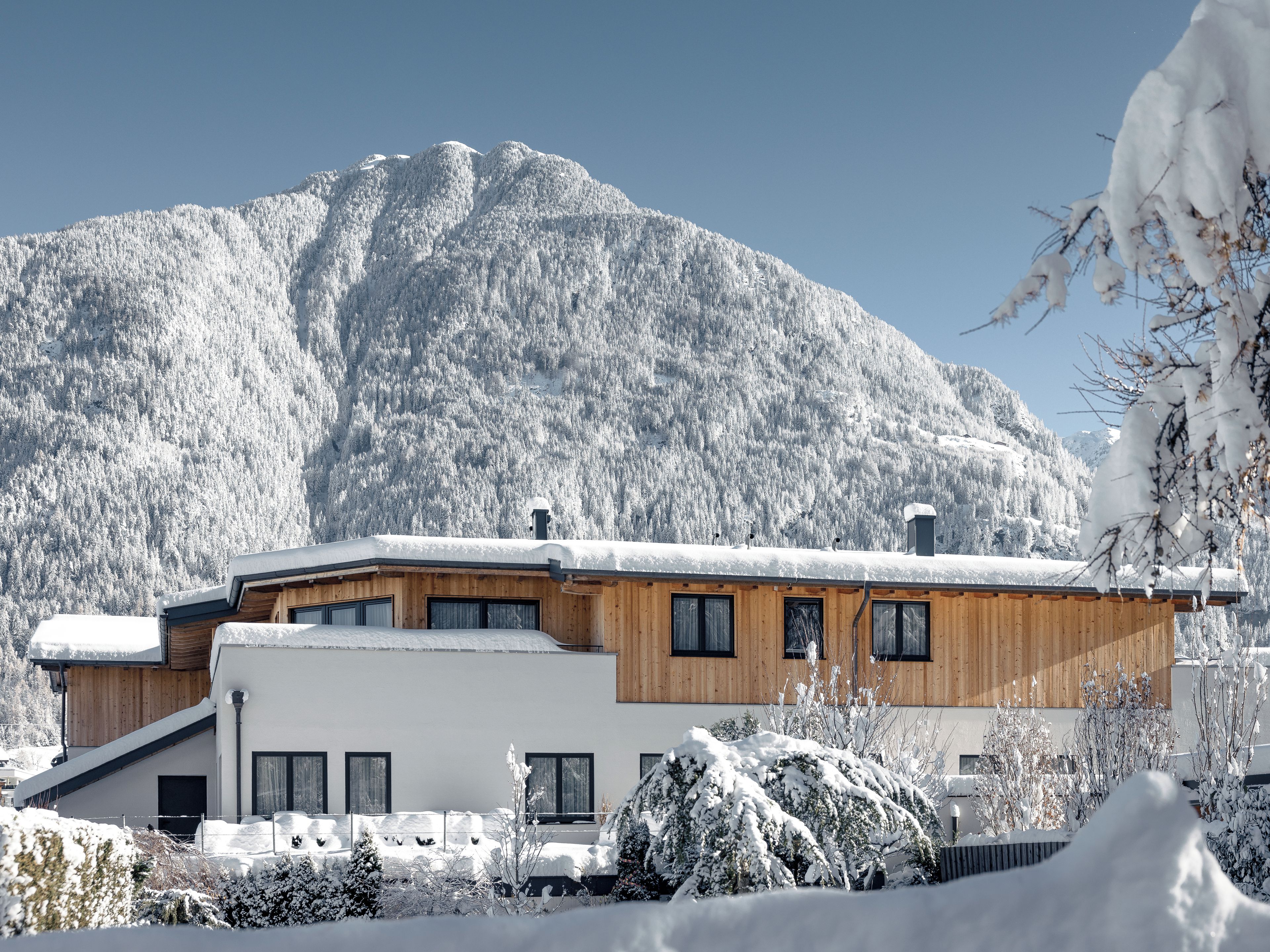 Un edificio moderno con fachada de madera y grandes ventanales, al pie de una imponente montaña nevada.