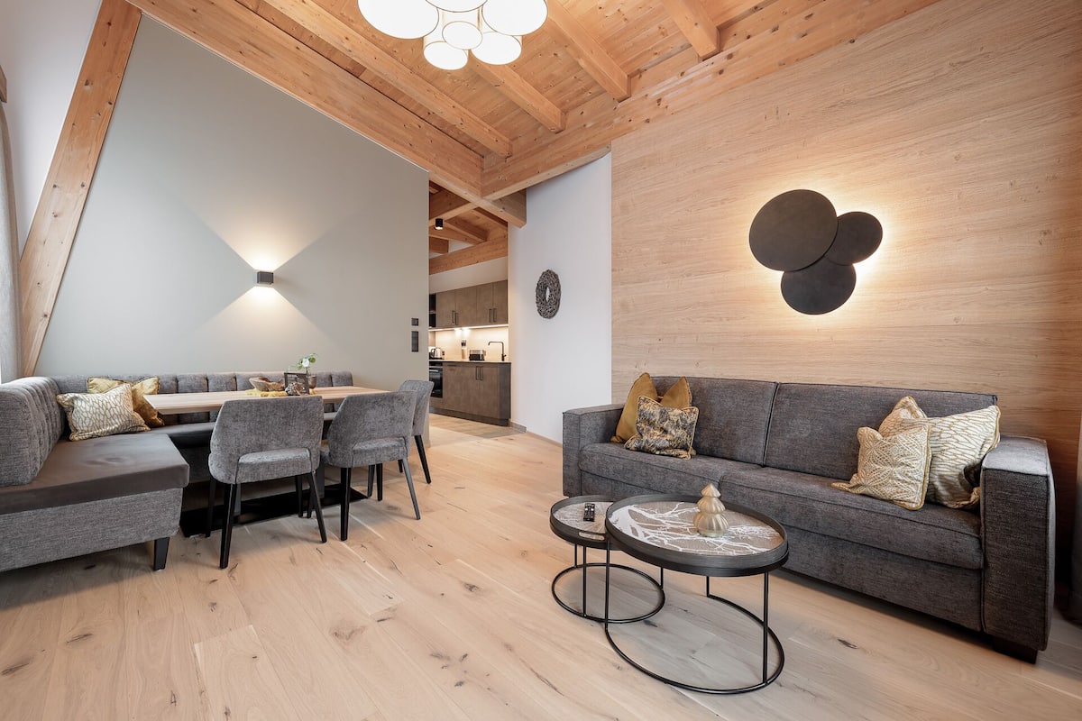 Ein modernes Wohnzimmer mit Essbereich, Holzbalkendecke und einer Küche im Hintergrund.