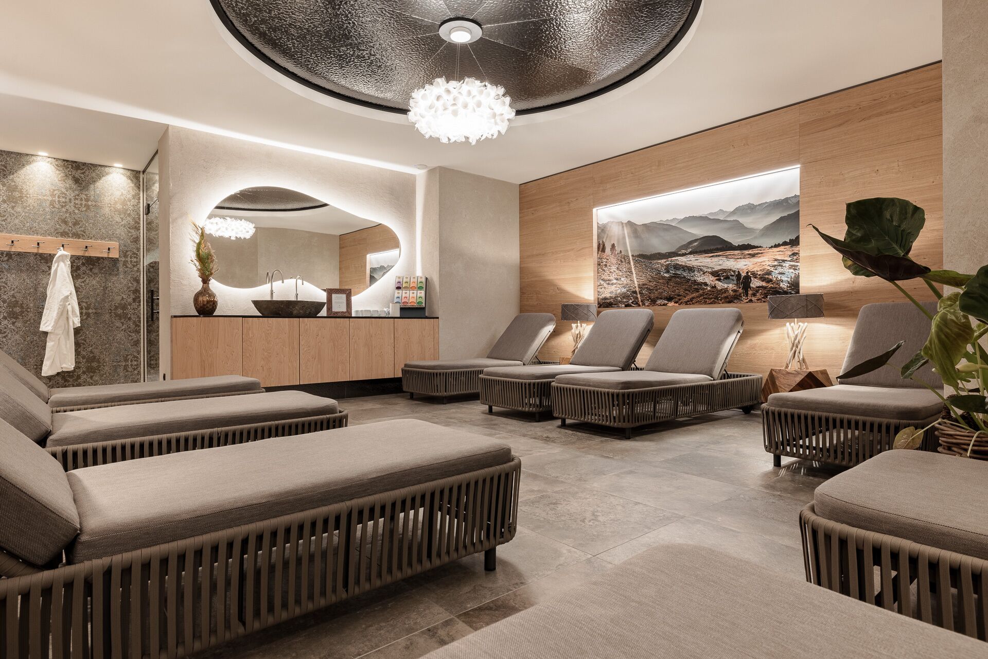 A modern spa room with a large mirror, a wooden wall with a scenic painting, and several cushioned seating areas.
