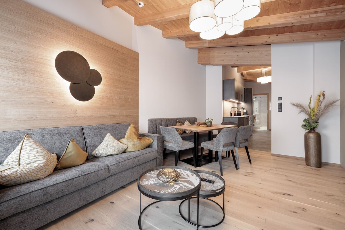 Ein modernes Wohnzimmer mit grauem Sofa, runden Couchtischen und einer Holzbalkendecke.