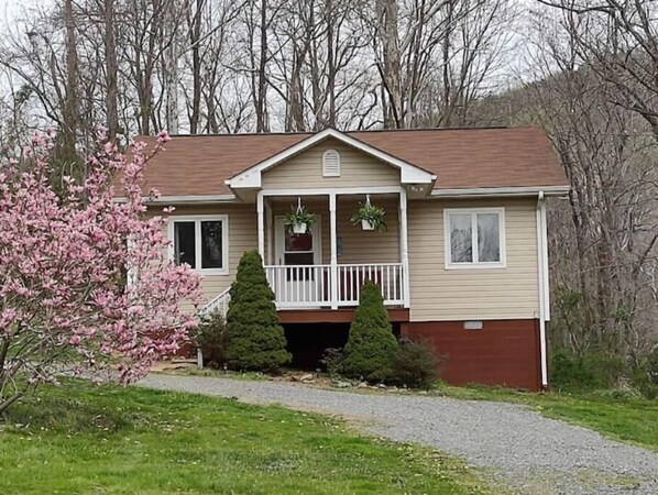 Stroll up to this charming home, featuring a cozy porch with a white railing and potted plants.