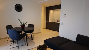 Ein modernes Wohnzimmer mit einer schwarzen Couch, einem Esstisch mit Stühlen und einer Topfpflanze.