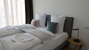 A neatly made bed with white linens, a grey headboard, and multiple pillows in various colors. - Apartment 22 (München)