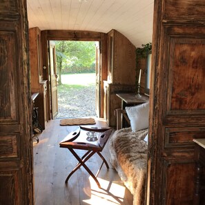 A rustic wooden room with a wooden table, a bench, and a view of a garden through an open door.