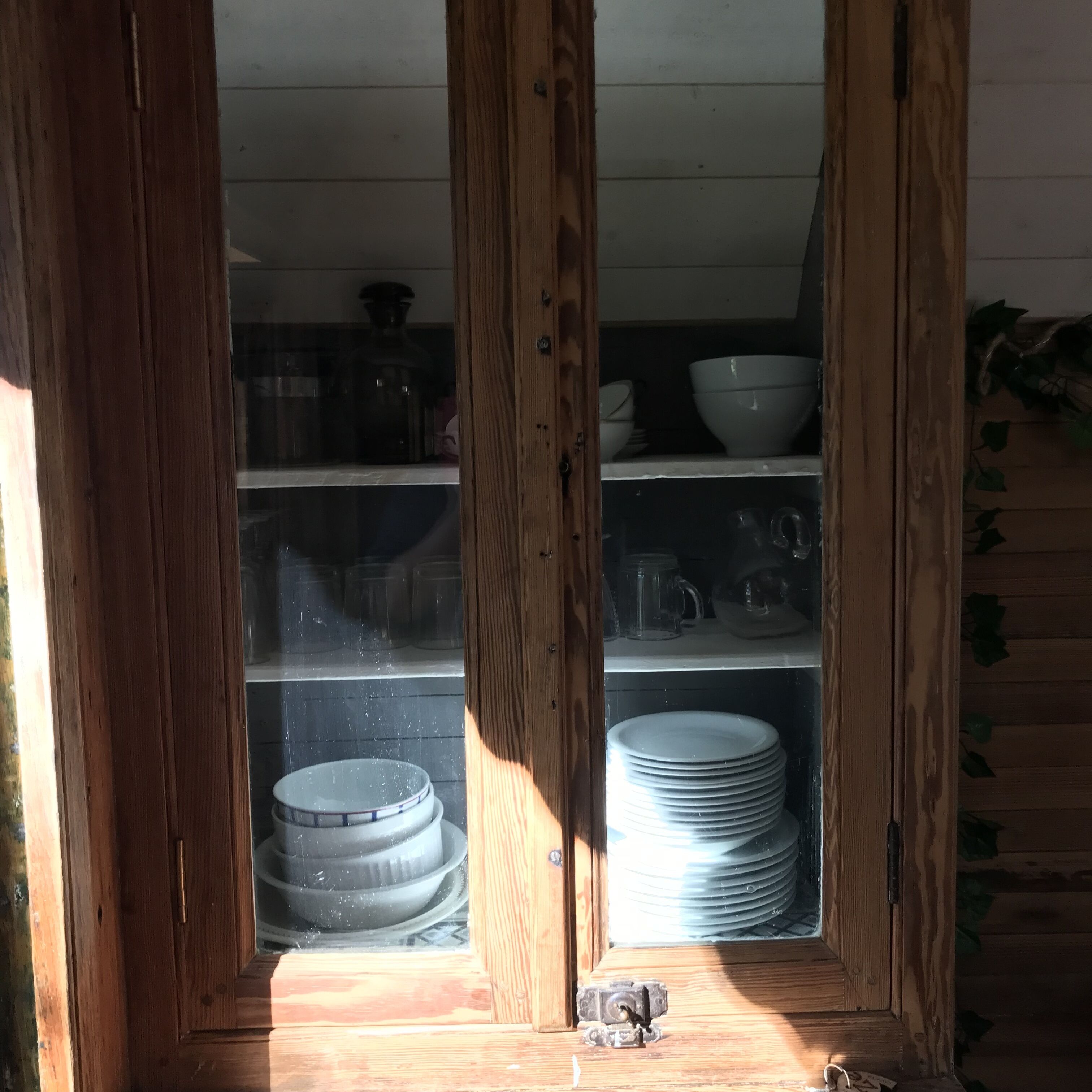 A wooden cabinet with shelves containing white dishes and a stack of plates.