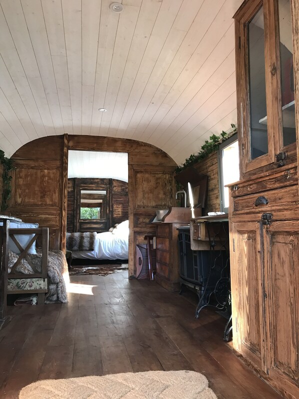 A rustic cabin interior with a wooden ceiling, a bed with white bedding, a desk with a chair, and a cabinet.