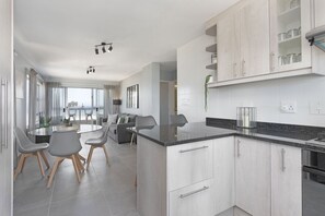 A modern kitchen with grey cabinets, a granite countertop, and stainless steel appliances. There is a dining area with a round table and chairs.