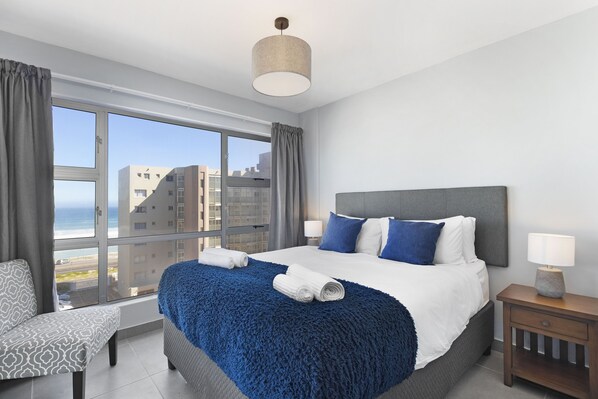 A modern hotel room with a large bed, a view of the city, and a window with curtains.