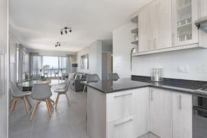 A modern kitchen with grey cabinets, a granite countertop, and a dining area with a round table and chairs.