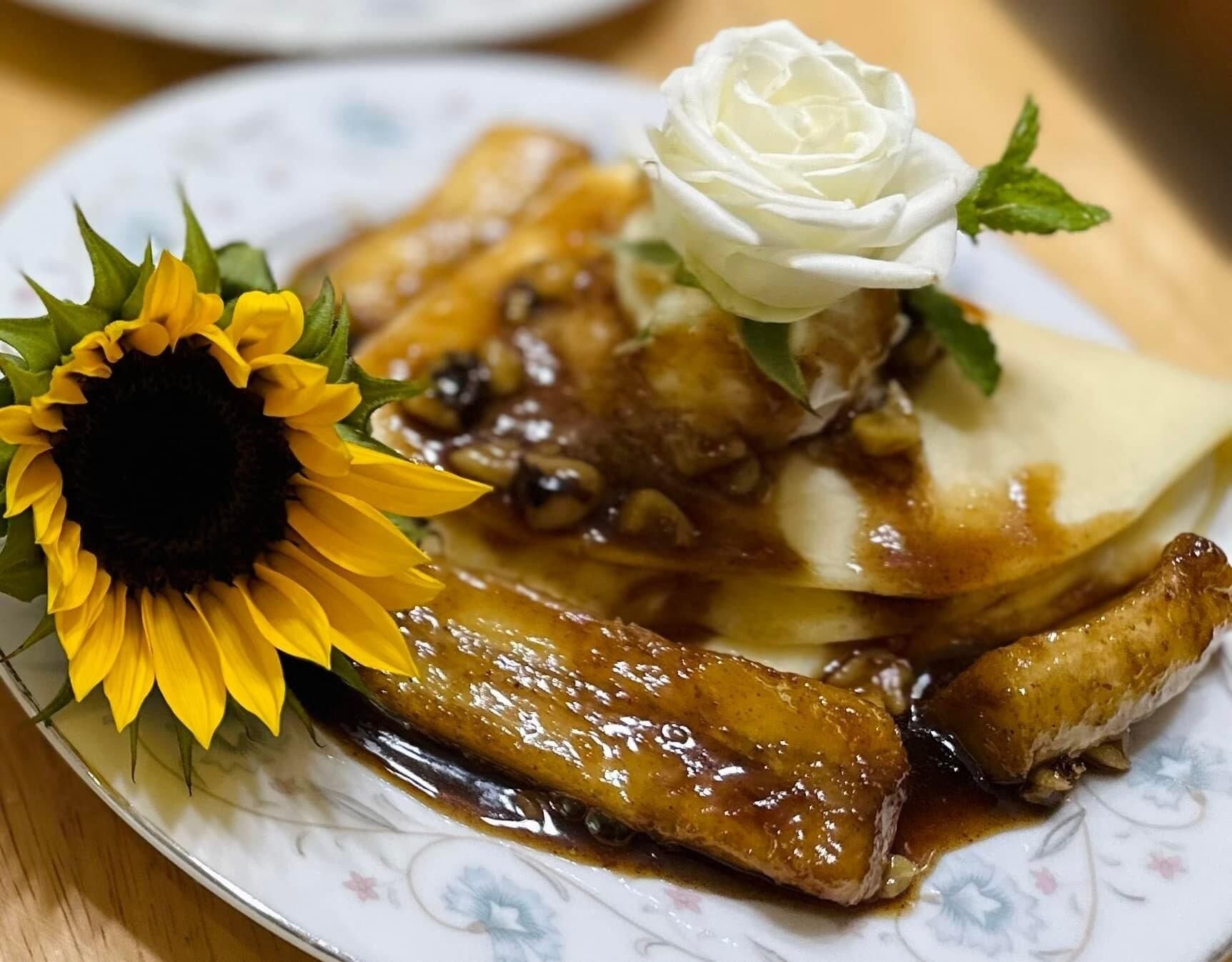 A plate with a dish of glazed meat, a white rose, and a sunflower.