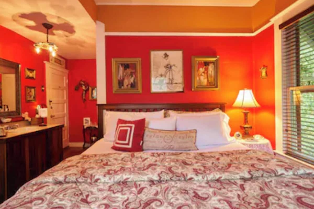 A bedroom with a large bed, a dresser, a mirror, and artwork on the wall.