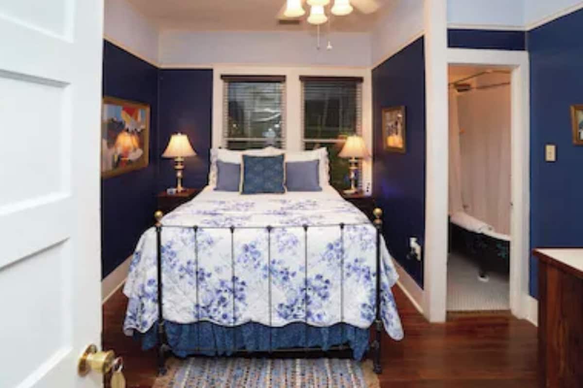 A bedroom with a bed, two bedside lamps, a window, and a door leading to another room.