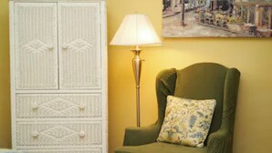 A room with a green armchair, a white cabinet with decorative panels, a floor lamp, and a painting on the wall. - Grady House Bed & Breakfast (High Springs)
