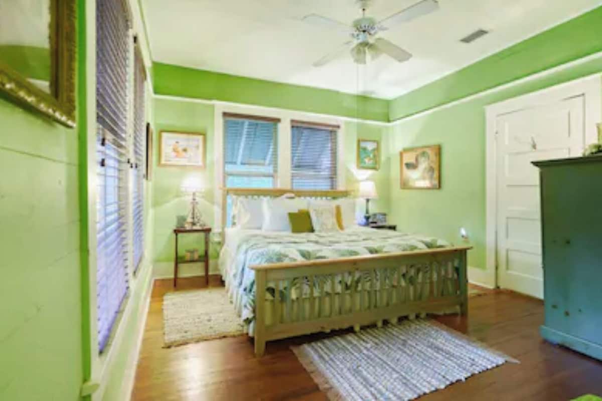 A bedroom with a bed, a nightstand, a dresser, a ceiling fan, and a window with blinds.