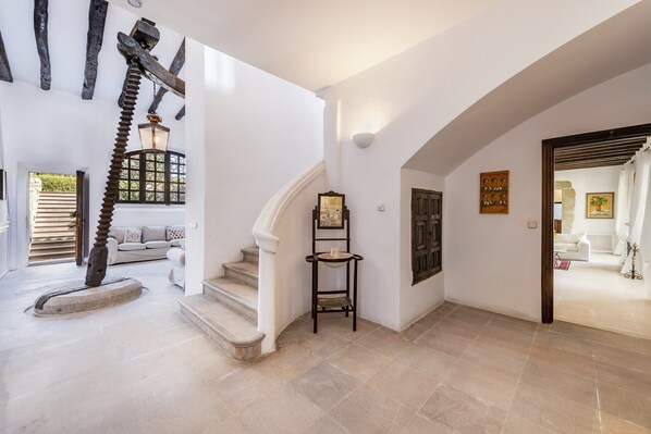 A spacious hallway with a staircase, a decorative spiral column, and a small table with a vase. - Villa Napolitano (Pollensa)