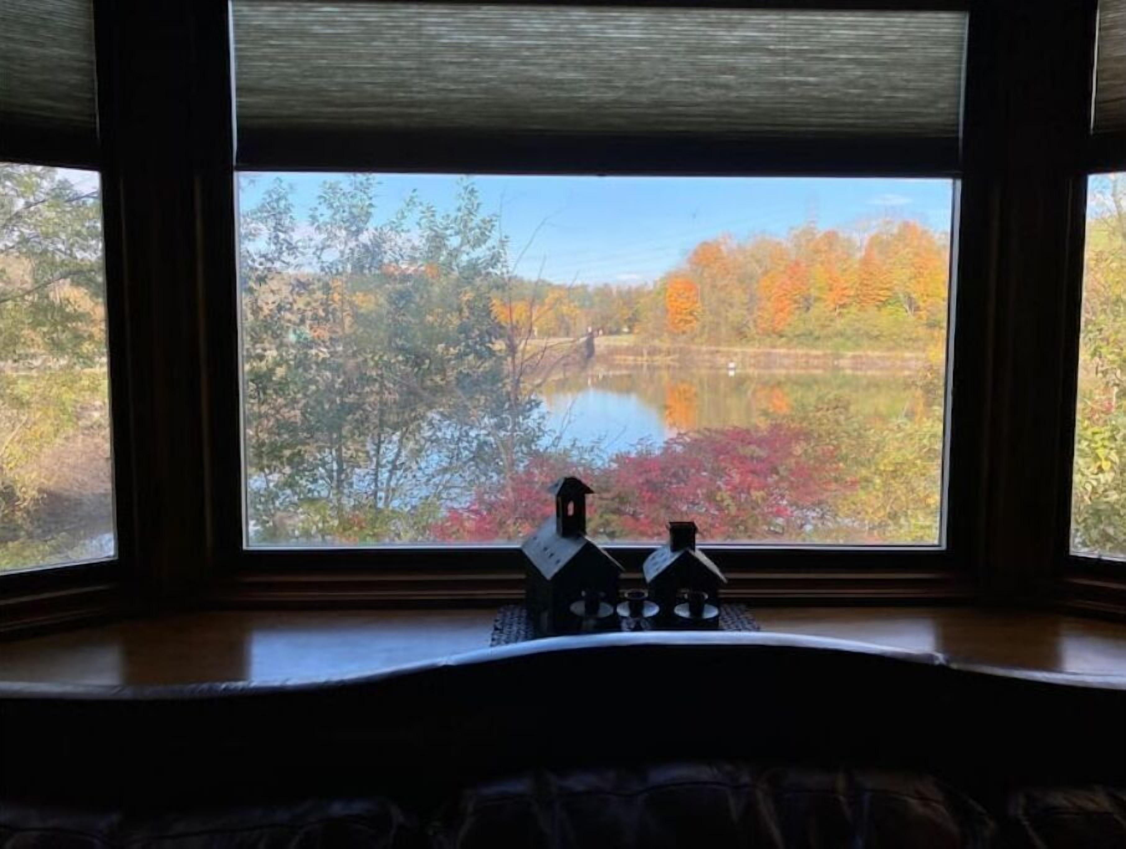Quarto com uma grande janela vista para um lago rodeado por folhagem outonal.