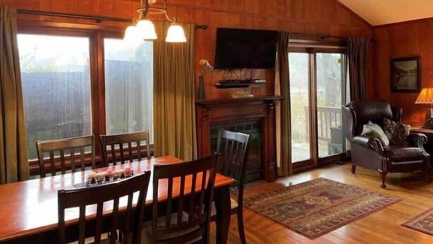Una sala de estar acogedora con detalles de madera, una chimenea, un televisor montado encima y un comedor con mesa y sillas.