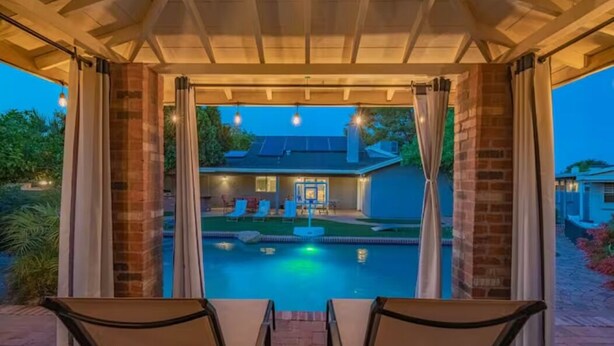 Zona exterior techada con piscina, mobiliario y vista a una casa.