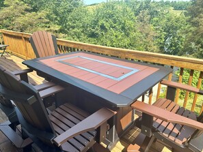 A deck with a table and chairs, surrounded by a wooden railing and lush greenery in the background. - Bright 2-bedroom lake view home (Scio)