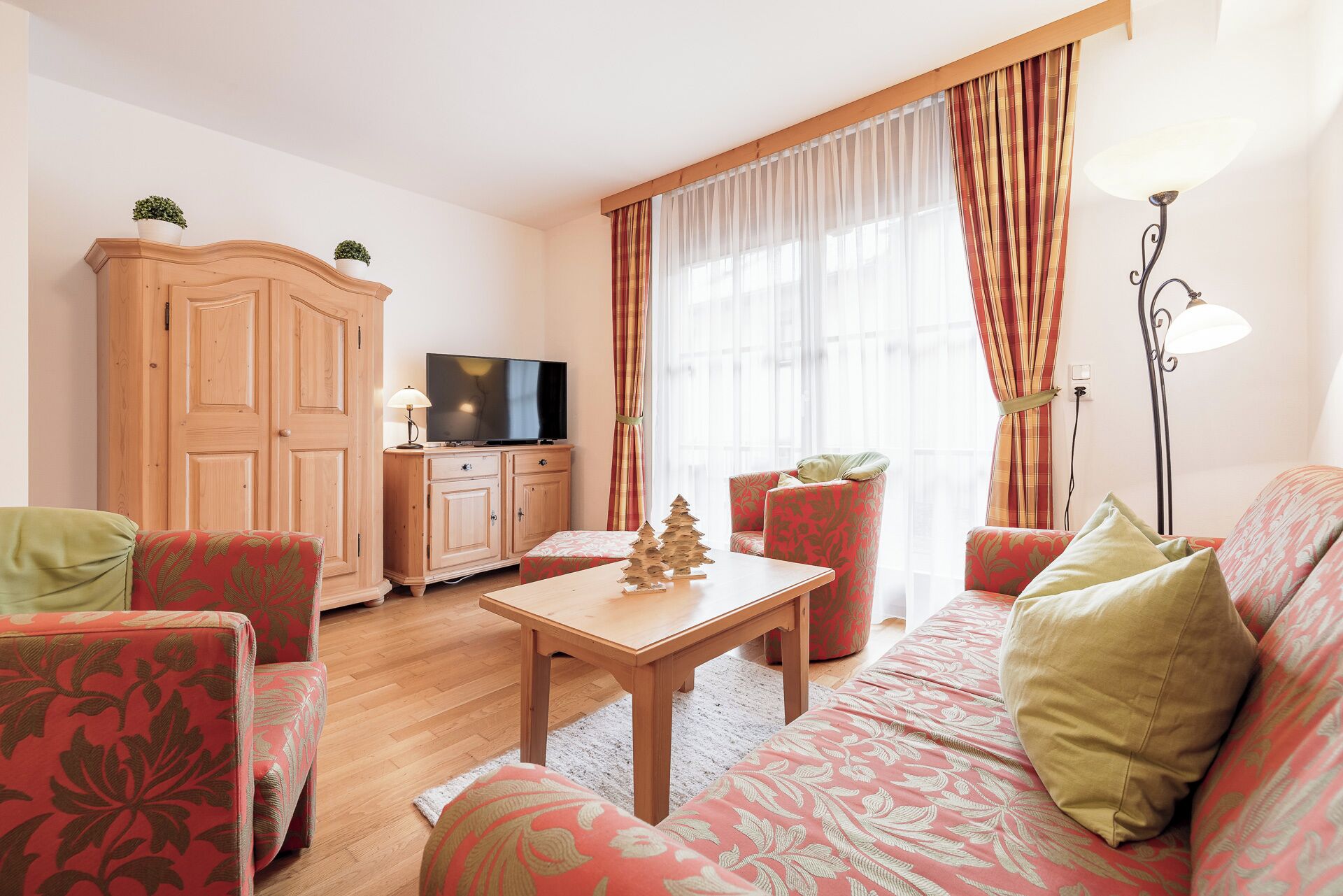 Una sala de estar acogedora con un aparador de madera, un televisor, un pequeño árbol de Navidad y muebles con motivos decorativos.