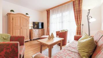 A cozy living room with a wooden cabinet, a television, a small Christmas tree, and patterned furniture.