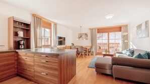 Eine moderne Küche mit Holzschränken, ein Essbereich mit Tisch und Stühlen und ein Wohnzimmer mit Sofa und Fernseher.