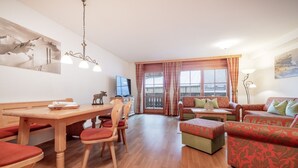 Ein geräumiger Wohnbereich mit einem Holzessttisch, roten Sitzmöbeln, einer Couch und einem Fernseher.