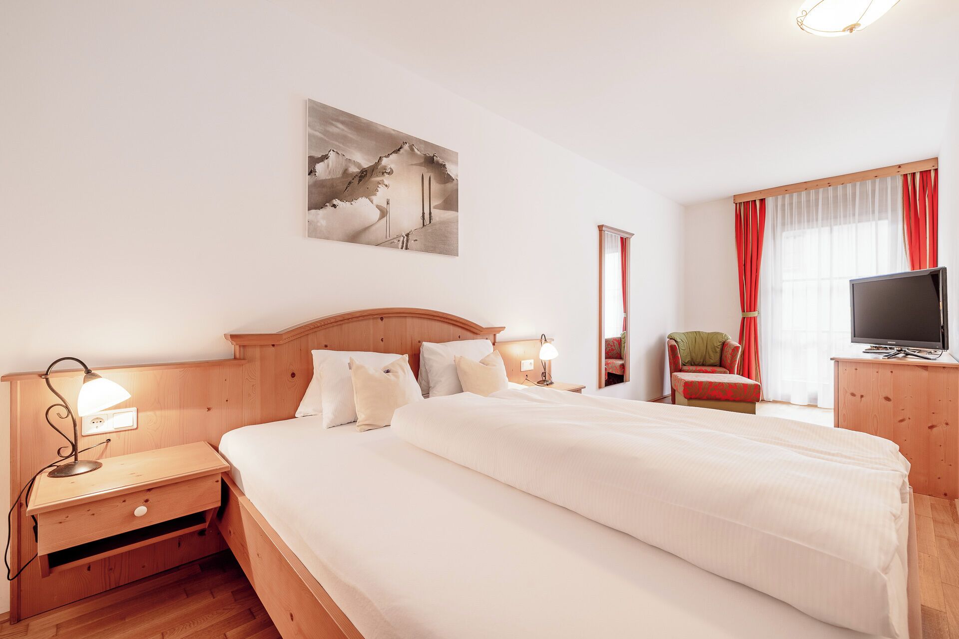 Ein Hotelzimmer mit einem großen Bett, Nachttischen, einem Schreibtisch mit Stuhl, einem Fernseher und einem Gemälde an der Wand.
