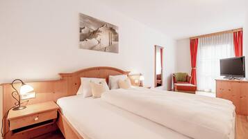 Ein Hotelzimmer mit einem großen Bett, Nachttischen, einem Schreibtisch mit Stuhl, einem Fernseher und einem Gemälde an der Wand.