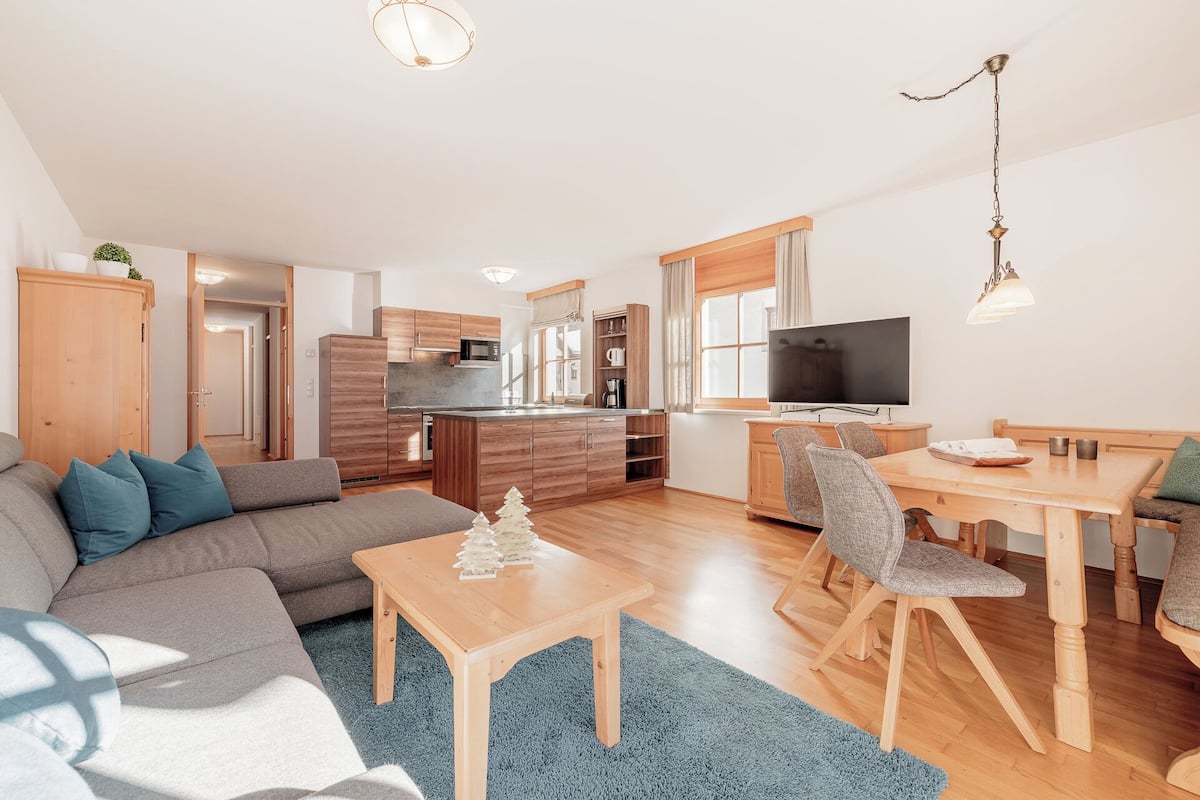 A modern living room with a sofa, coffee table, and a dining area with chairs and a TV.
