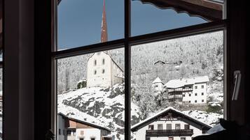 Blick aus dem Fenster auf ein verschneites Bergdorf mit traditionellen Häusern und einem Kirchturm.