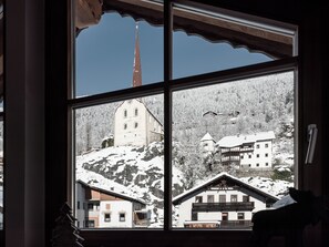 A window view of a snow-covered mountain village with traditional buildings and a church steeple. - MYALPS Historical (Oetz)