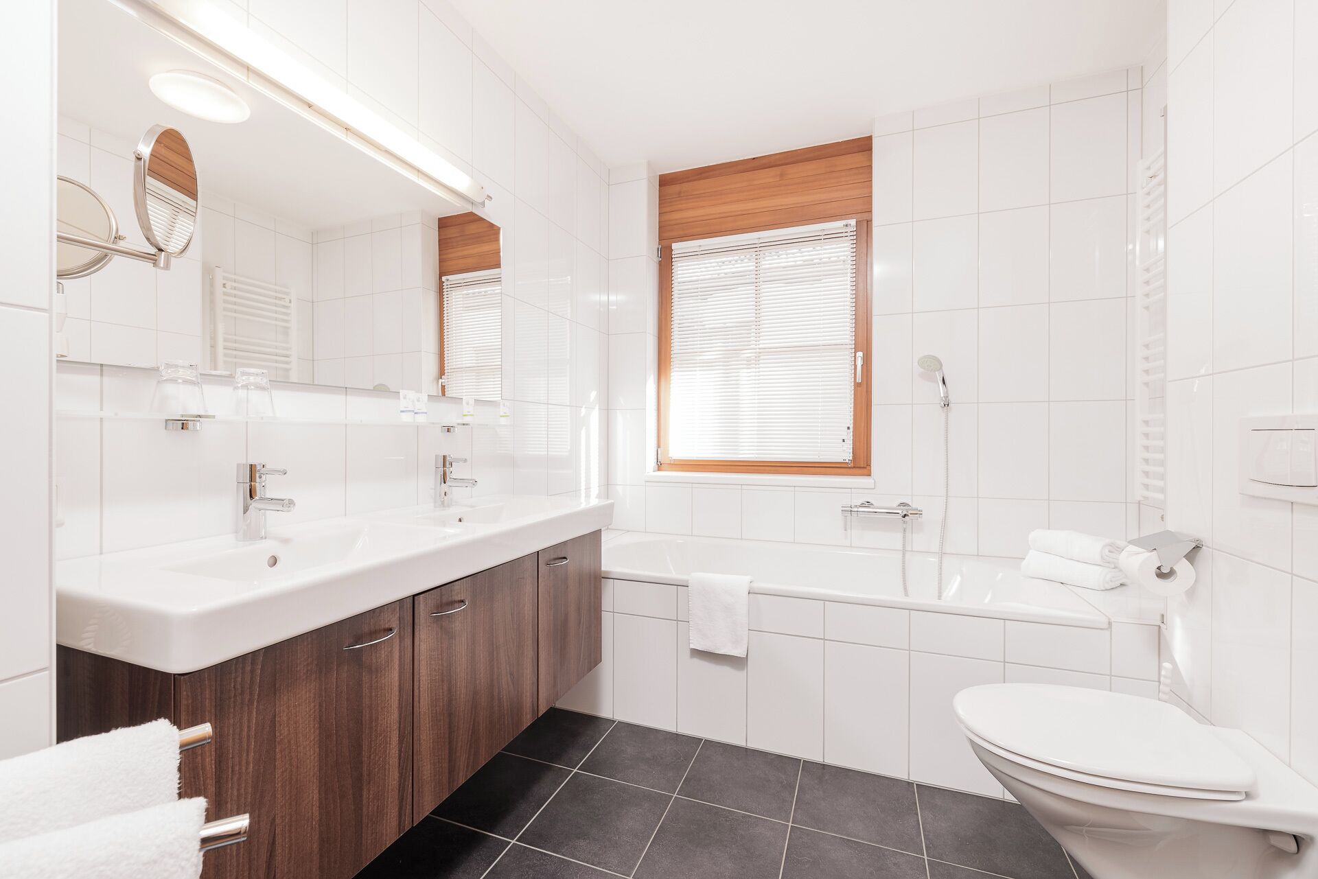 A modern bathroom with a double sink vanity, a bathtub, and a toilet.