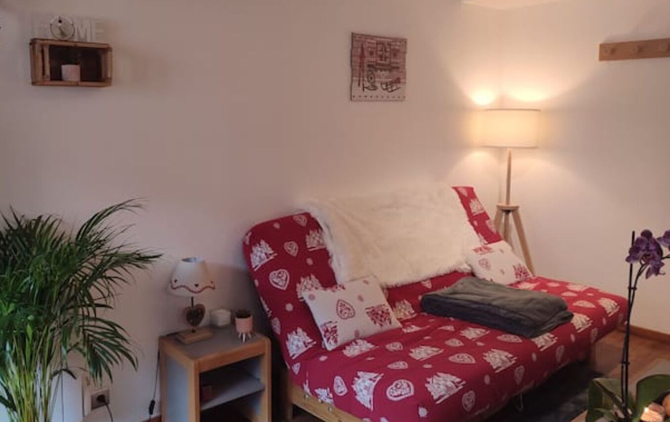 Una habitación acogedora con un sofá rojo estampado, una lámpara y una mesita con una planta.
