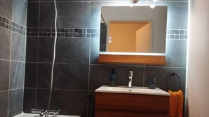 A modern bathroom with dark tiles, a white sink, and a mirror above it. - Grand Chalet (Brides-les-Bains)