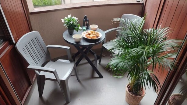 A small balcony with a table, chairs, a potted plant, and a bowl of food. - Grand Chalet (Brides-les-Bains)