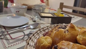 A dining table with a basket of pastries, a bowl, a spoon, and a candle. - Grand Chalet (Brides-les-Bains)