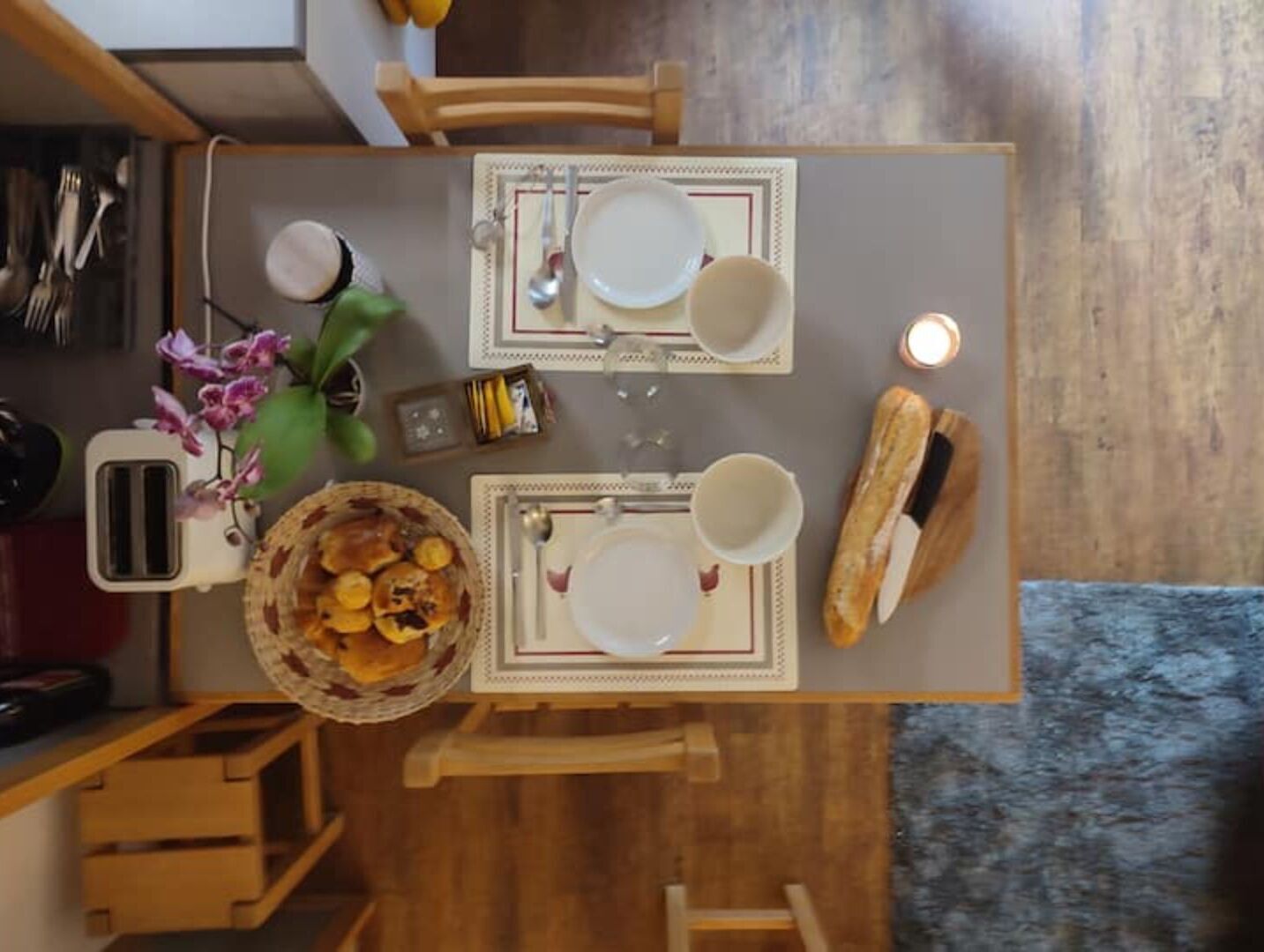 Una mesa de comedor dispuesta con platos, tazas y una cesta de comida, rodeada de sillas.