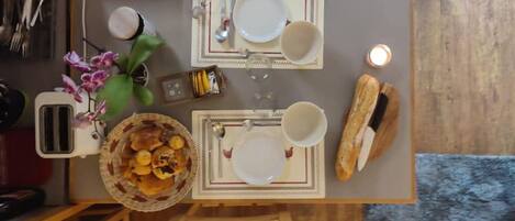 Una mesa de comedor dispuesta con platos, tazas y una cesta de comida, rodeada de sillas.
