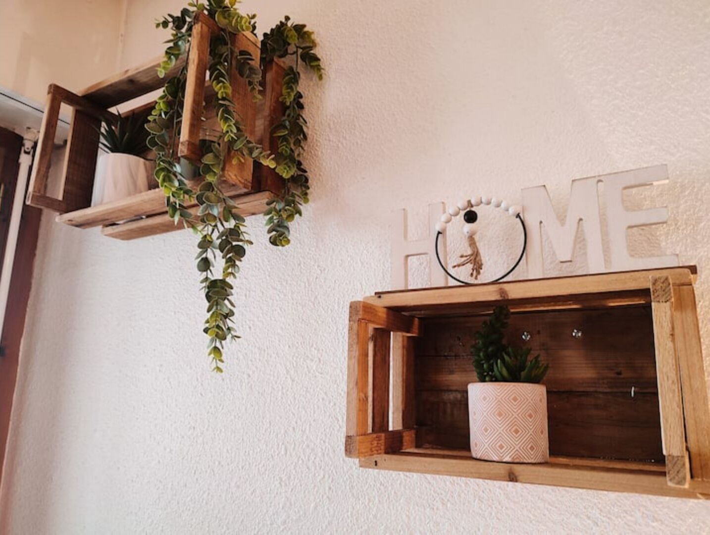 Una pared con dos estantes de madera, uno con una planta en maceta y el otro con un adorno y la palabra 'HOME'.