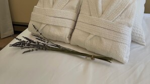 A bed with two white bathrobes and a lavender sprig.