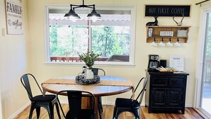 A dining area with a wooden table, black chairs, a hanging light fixture, a window with a view, and a coffee station.