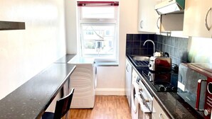 A compact kitchen with a window, a sink, a stove, and a microwave. - Lovely 2-bed Tree-hole in Northolt Southharrow (Northolt)