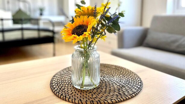 A clear view of a living room with a sofa, a coffee table with a vase of flowers, and a staircase in the background. - Lovely 2-bed Tree-hole in Northolt Southharrow (Northolt)