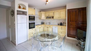A modern kitchen with white cabinets, a glass dining table, and a built-in oven. - Bright cocoon with terrace and sea view (Saint-Raphaël)