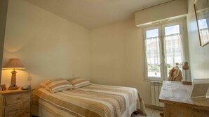 A bedroom with a bed, a nightstand, a lamp, a window with curtains, and a dresser. - Bright cocoon with terrace and sea view (Saint-Raphaël)